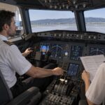Dos pilotos practican el manejo manual de una cabina de simulación con una lista de procedimientos en papel.