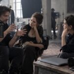 Director y dos profesionales conversan junto a una cámara de cine y un portátil cerrado sobre una mesa.