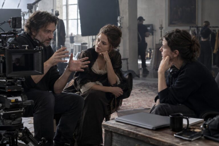 Director y dos profesionales conversan junto a una cámara de cine y un portátil cerrado sobre una mesa.